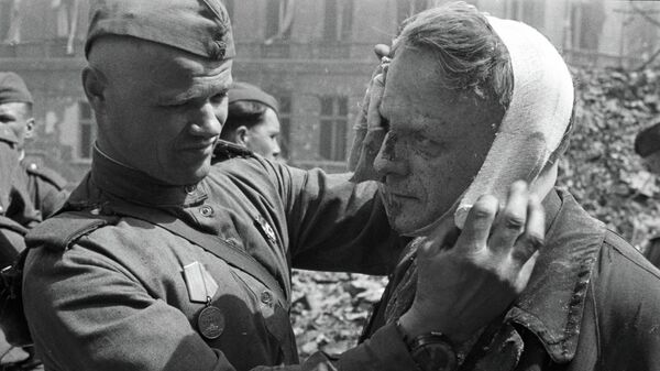 Советский солдат делает перевязку раненому в голову берлинцу