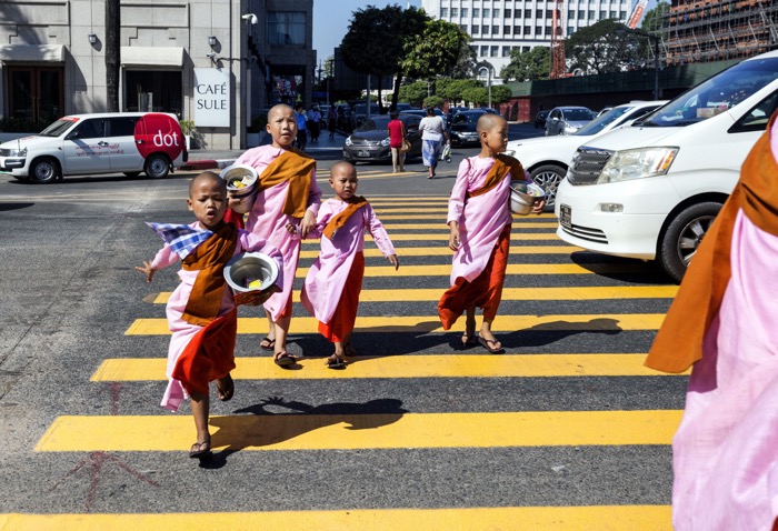 A group of children in traditional clothing crossing a busy street - street photography