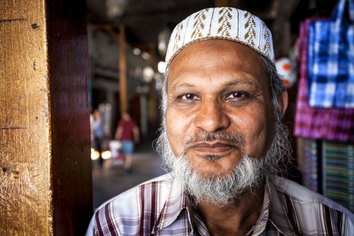Close up street photography portrait of a man with white beard and hat in a market