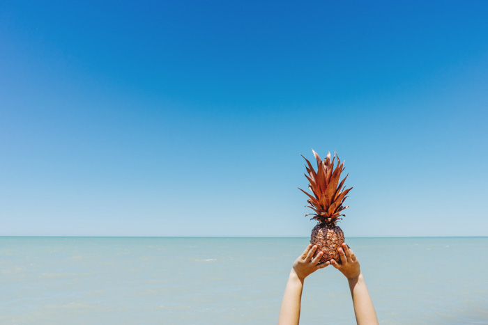 A minimal photography composition of a person holding a pineapple against a blue sea and sky - golden ratio vs rule of thirds