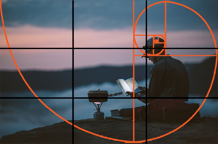 A photographer sitting on rocks in low light, with both the golden ratio and rule of thirds grid overlayed