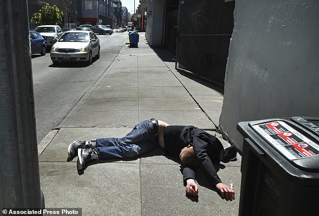 In this photo taken on April 26, a man lies on the sidewalk beside a recyclable trash bin in San Francisco