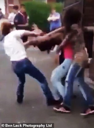 The girl is held back by two other while another girl in a white jumper punches her