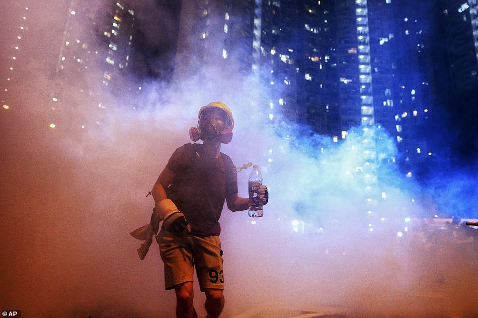 Officials said they arrested more than 20 people for offences overnight including unlawful assembly and assault. Pictured is one protester in the midst of tear gas during a confrontation with police last night