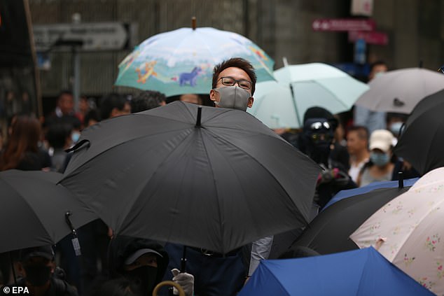 Shielded: Pro-democracy protesters block a road during a lunchtime flash mob in the centre of Hong Kong today, some of them hiding behind umbrellas
