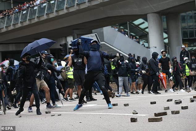 Clashes: A pro-democracy protester throws stones to block a road during a lunchtime flash mob in the heart of Hong Kong