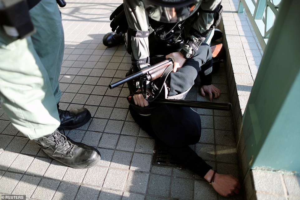 A police officer holding a shotgun holds an anti-government protester to the ground amid a protest at the Sheung Shui shopping mall in Hong Kong