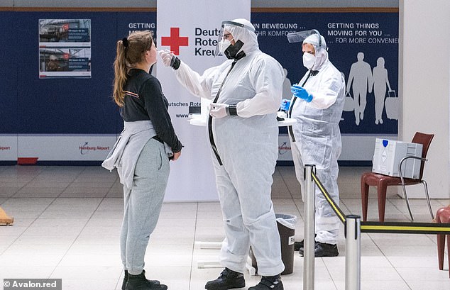A German Red Cross worker wearing protective gear and a face shield takes a swab from a traveller at Hamburg Airport after compulsory tests were introduced in Germany
