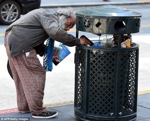 A homeless man digs in the trash while talking to himself in downtown San Francisco, California on June 28