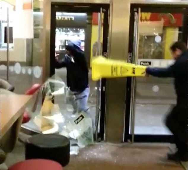 A second security guard comes to the aid of his colleague, using a yellow cone as a weapon