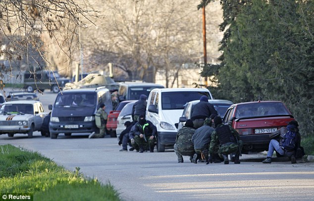 Members of pro-Russian self-defence units take cover behind cars outside the military base while Russian forces take it over