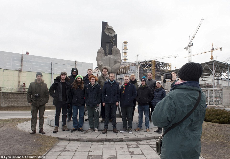 A tour group poses for a photo in front of a communist monument in the deserted city, with the nuclear power plant in the background