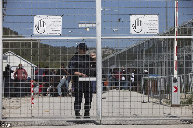 A Police officer closes the gate of Moria camp as refugees behind her protest against the EU- Turkey deal