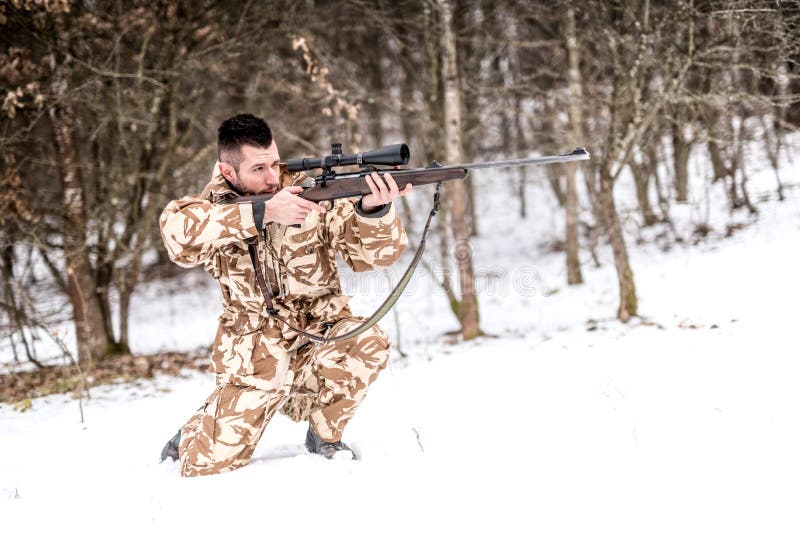 Hunter with sniper rifle aiming and shooting during winter stock photo