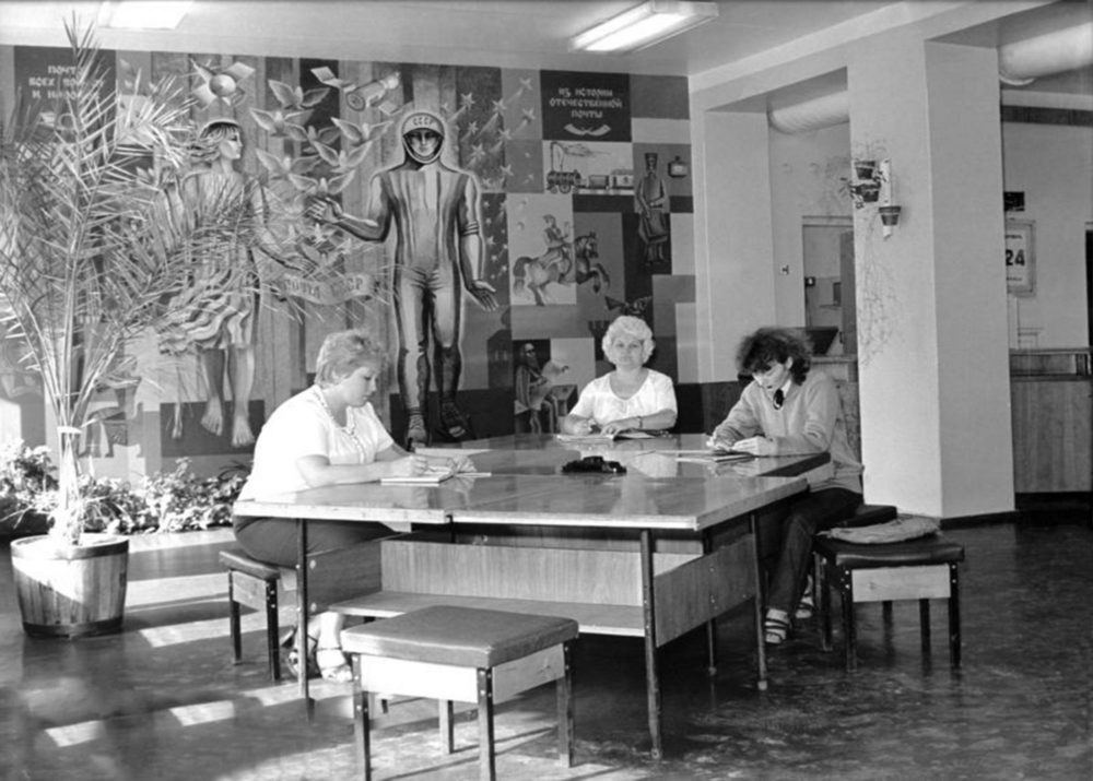 A group of ladies in the post office, with the panting on the wall behind