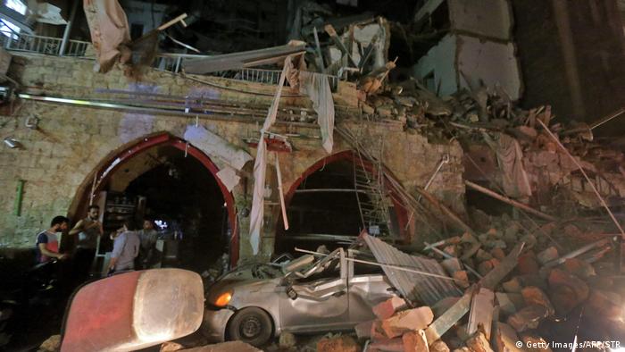 People stand by building and car in ruins in the evening
