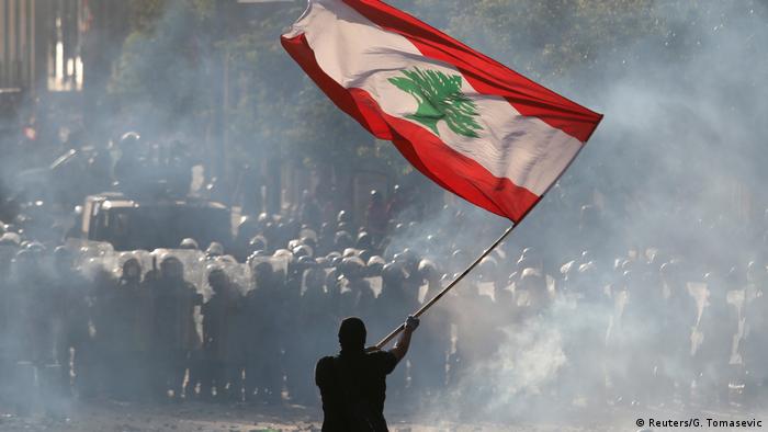 A protesters lifts the Lebanese flag in front of police (Reuters/G. Tomasevic)